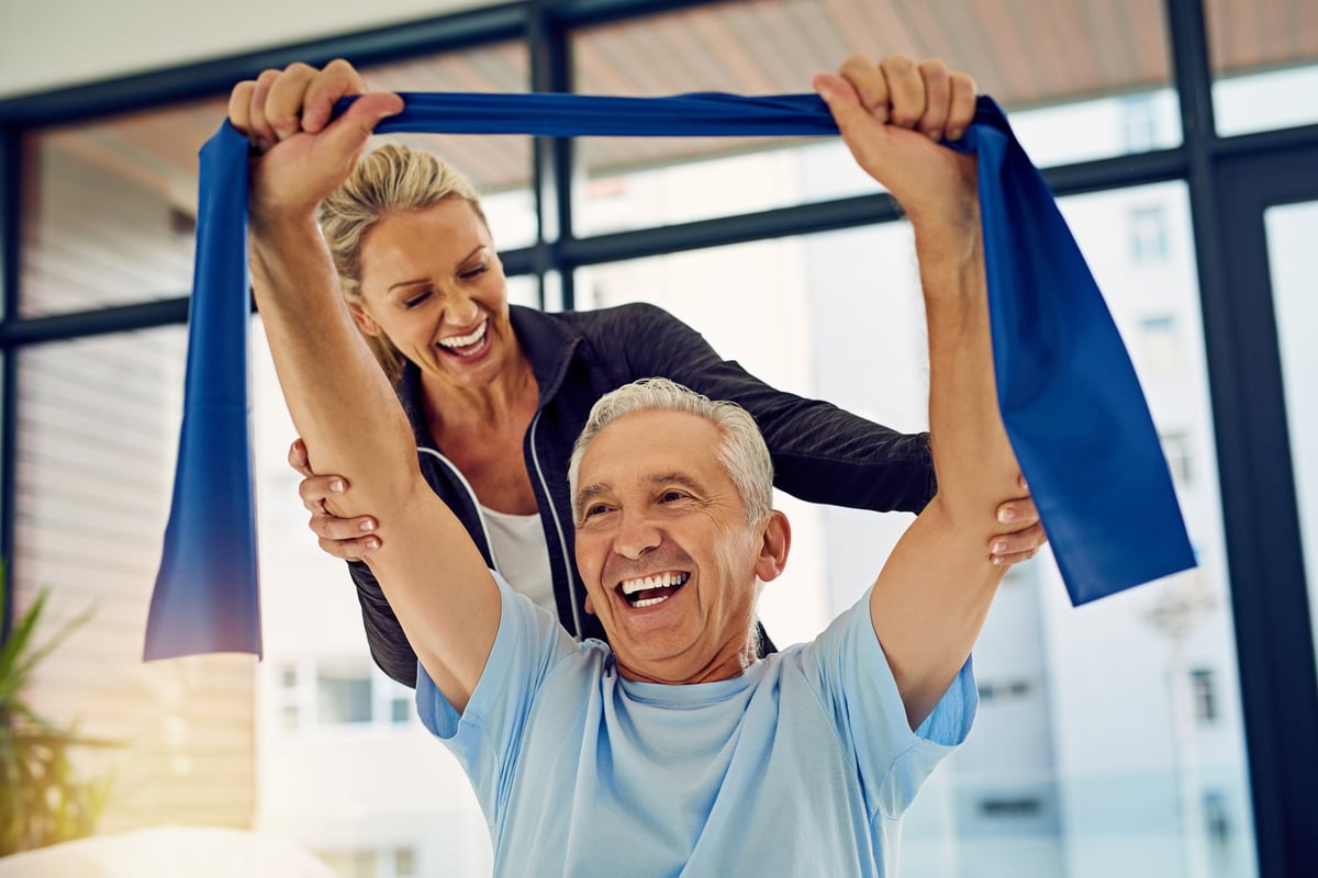 Trainer helping a senior client stretch with a resistance band